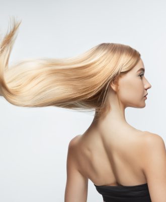 Beautiful model with long smooth, flying blonde hair isolated on white studio background. Young caucasian model with well-kept skin and hair blowing on air. Concept of salon care, beauty, fashion.