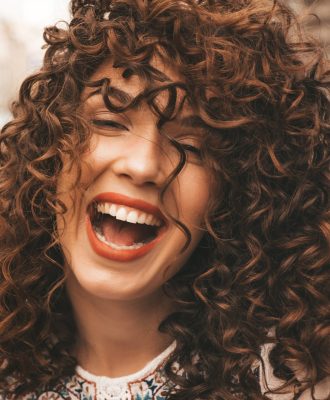 Portrait of beautiful smiling model with afro curls hairstyle.Sexy carefree girl posing in the street background.Trendy  and funny woman shows positive emotions
